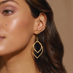Close-up of a model wearing the Transformed by Light Lotus Linear Earrings, highlighting their shimmering gold design. This spiritual jewelry piece serves as a beautiful talisman for protection and embodies qualities of the sun and moon, enhancing yoga and meditation rituals.