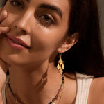 A close-up of a model wearing the Adorned with Light Chandelier Earrings, showcasing the beautiful hammered 18kt gold plate petals. This spiritual jewelry piece symbolizes new beginnings and is perfect for meditation and meaningful manifestation. Ideal for those who appreciate talismans and seek protection in their spiritual journey.