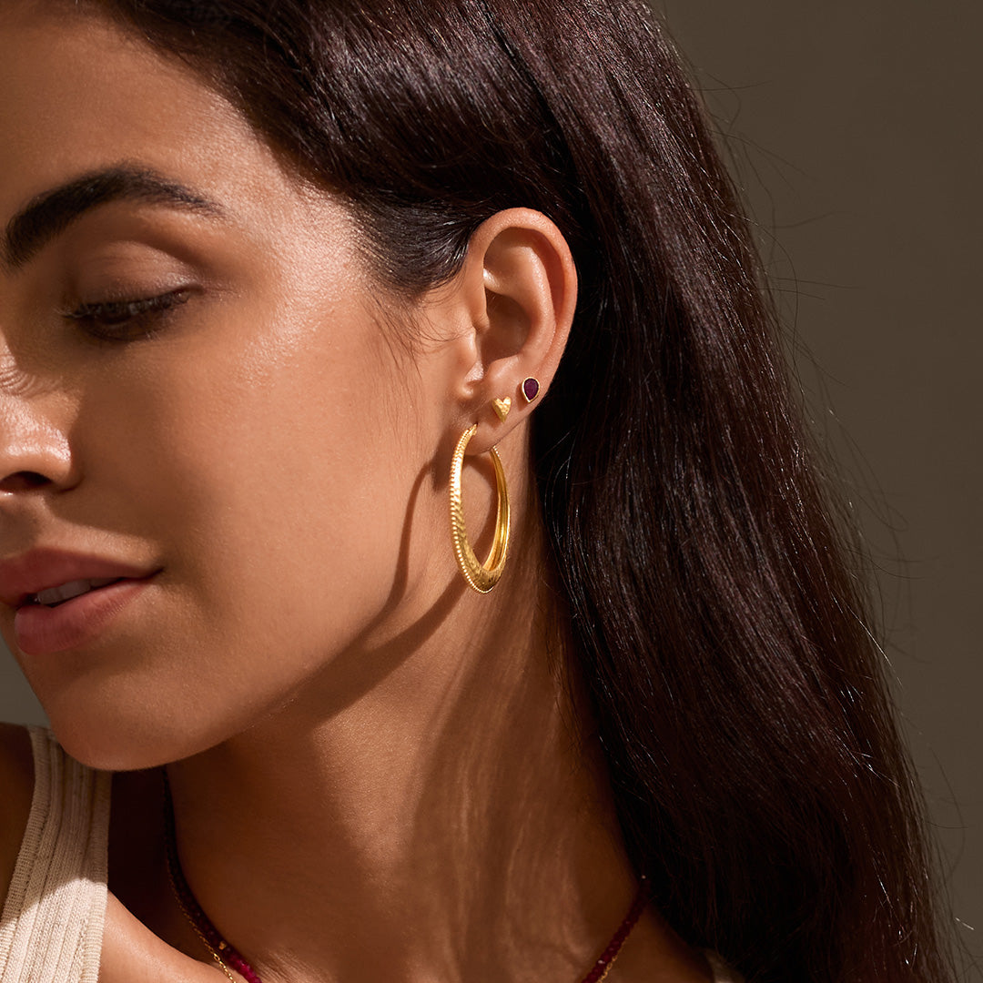 A model showcasing All Love Garnet Stud Earrings alongside gold hoop earrings, highlighting the garnet's significance in spiritual jewelry and protection while enhancing your meditation and yoga practices.