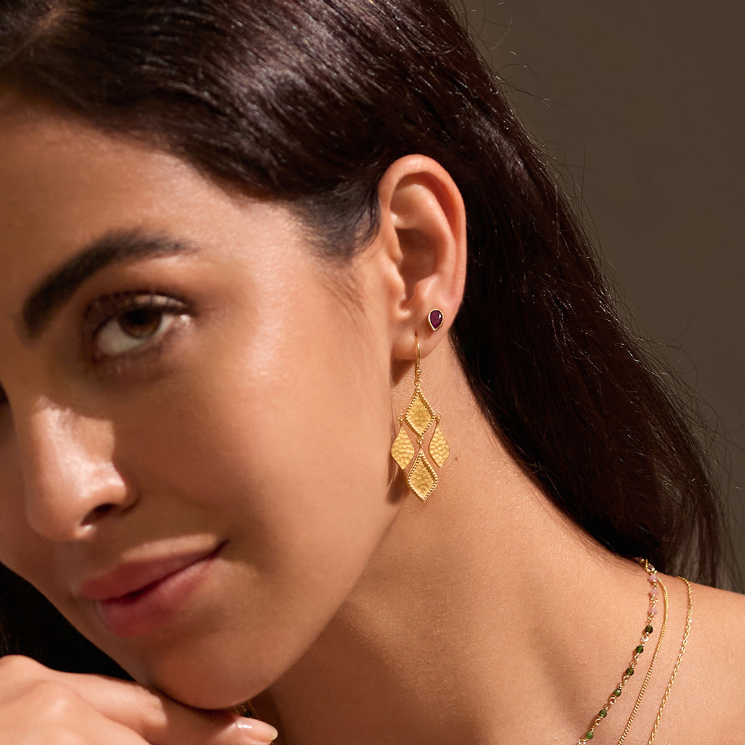 A close-up of a model wearing All Love Garnet Stud Earrings paired with intricate gold earrings, emphasizing the earrings' roles as talismans for love and meaning in spiritual life and yoga.