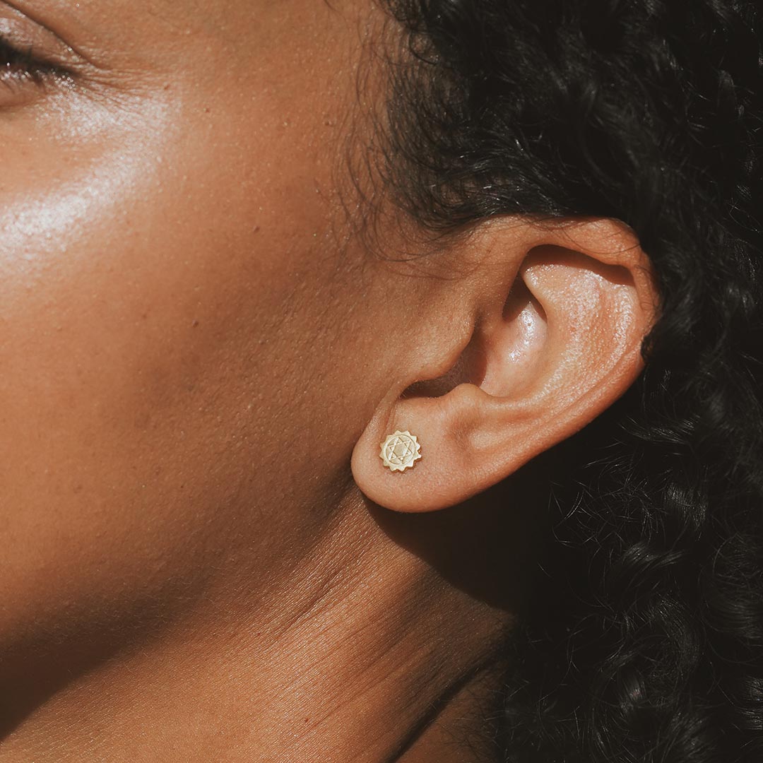 Close-up of Heart Chakra Stud Earrings worn on an ear, highlighting the gold plating and design. This spiritual jewelry is not only stylish but acts as a protective charm, perfect for daily wear in yoga practices and meditation, aligning with the sun and moon energies.