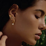Close-up of a woman wearing True Self Green Amethyst Earrings along with other delicate jewelry pieces. The green amethyst and rose quartz earrings reflect the essence of spirituality and personal meaning, making it a great talisman for zodiac lovers and those on a journey of self-discovery and protection.