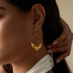 A model wearing Fluttering Petals Gold Earrings that elegantly accentuates her style. These earrings embody the essence of spiritual jewelry, blending fashion with meditation and the significance of talismans. Perfect for yoga enthusiasts and those interested in zodiac meanings and manifestation.