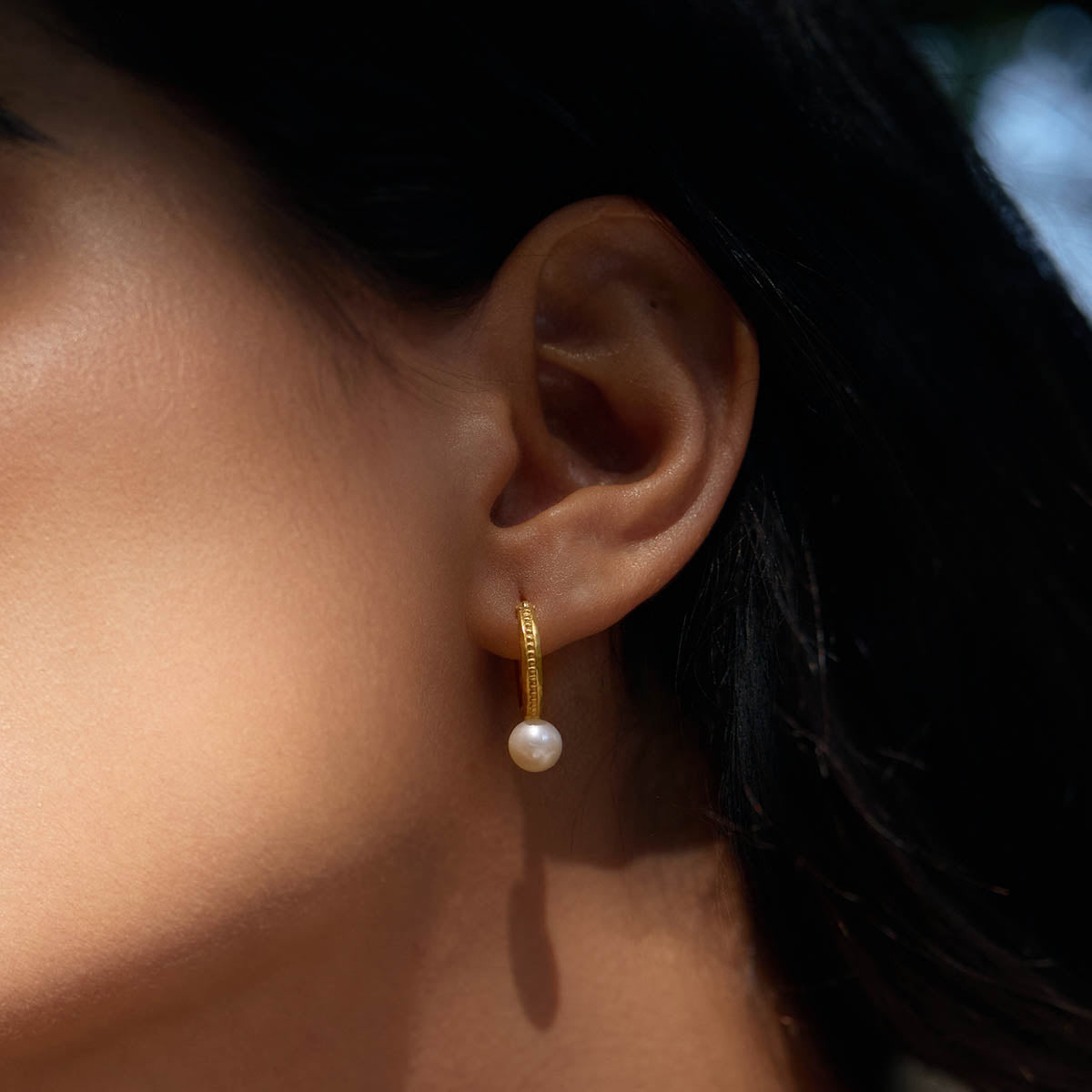 Close-up of Nature's Harmony Pearl Hoop Earrings displayed by a model, highlighting the textured gold and smooth freshwater pearl. Ideal for spiritual practices, this meaningful jewelry enhances protection and embodies the essence of yoga and zodiac energy.