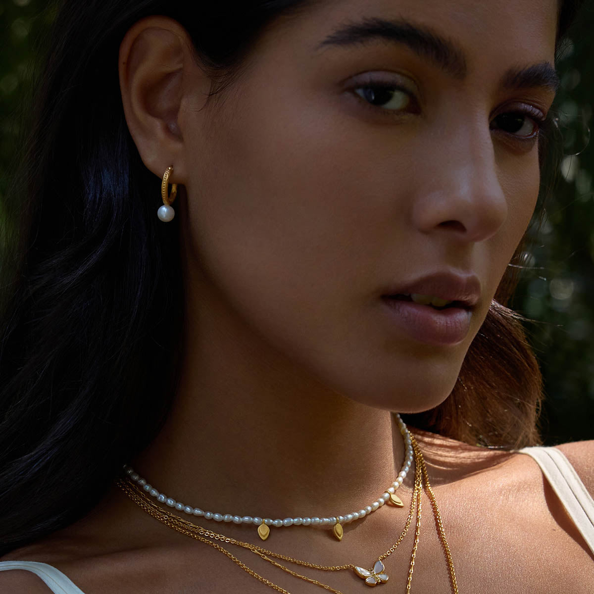 Model adorned with Nature's Harmony Pearl Hoop Earrings, layered with other beautiful gold jewelry. This collection reflects a deep connection to the sun and moon, offering meditation and manifestation insights through each meaningful piece.