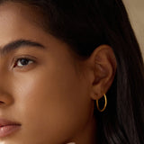 Close-up of a model wearing Textured Gold Medium Hoop Earrings, highlighting their elegant look and minimalist appeal. These hoops are part of a spiritual jewelry collection, perfect for yoga enthusiasts and those seeking talismans that embody meaning and connection to the sun and moon.