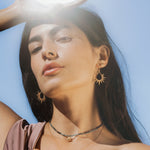 A woman poses confidently in bright daylight wearing Guiding Star Celestial White Topaz Stud Earrings, radiating energy and grace, ideal for those inspired by sun, moon, and yoga, connecting deeply with spirituality and personal meaning.