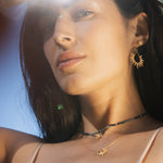 A model showcases the Lucent Glow Starburst Linear Drop Earrings, adorned with 18kt gold plating, reflecting spirituality and inspiration under the sun. These earrings are perfect for meditation and meaningful styles, symbolizing protection and manifestation, ideal for yoga enthusiasts seeking a zodiac-inspired look.