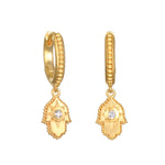 Gold-tone huggie hoop earrings with hamsa hand charms featuring white crystal centers.