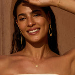 Gold-toned necklace with circular sun-shaped pendant worn close to the collarbone.