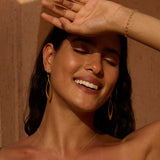 Gold lotus petal drop earrings worn on model with dark hair against warm background.