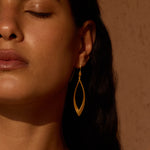 Gold-toned lotus petal drop earrings with elongated pointed oval shape worn on model with dark hair.