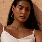 Teardrop hoop earrings with turquoise beads and gold-tone metal accents worn on model.