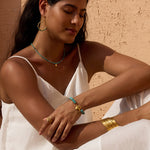 Pair of turquoise beaded hoop earrings with textured gold finish worn on model against tan textured wall.