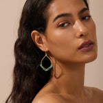 Gold-toned drop earrings with turquoise beaded teardrop shape, worn by a person with dark hair against a neutral background.
