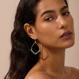 Gold-toned drop earrings with turquoise beaded teardrop shape, worn by a person with dark hair against a neutral background.