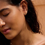 Gold-tone dragonfly stud earrings with clear gemstone accents worn on earlobe.