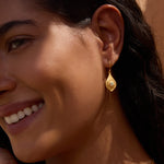 Gold teardrop earring with opal stone and sun ray pattern worn on ear.