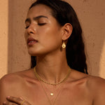 Pair of gold teardrop earrings with iridescent opal stones, displayed on model wearing matching gold necklaces.
