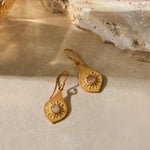Pair of gold teardrop earrings with sun motif and opal stone centers on wire hooks.