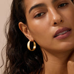 Gold-toned hammered hoop earrings with textured surface worn on model's ears.