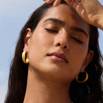 Gold-tone hoop earrings with hammered texture worn on model's ears.