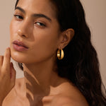 Gold-tone hammered hoop earrings worn on model's ears against neutral background.