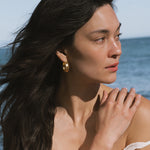 Gold hoop earrings with textured surface worn by person with long dark hair.