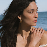 Gold hoop earrings with textured surface worn by person with long dark hair.