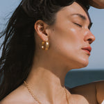 Gold hoop earrings with textured surface worn on model's ears in profile view.
