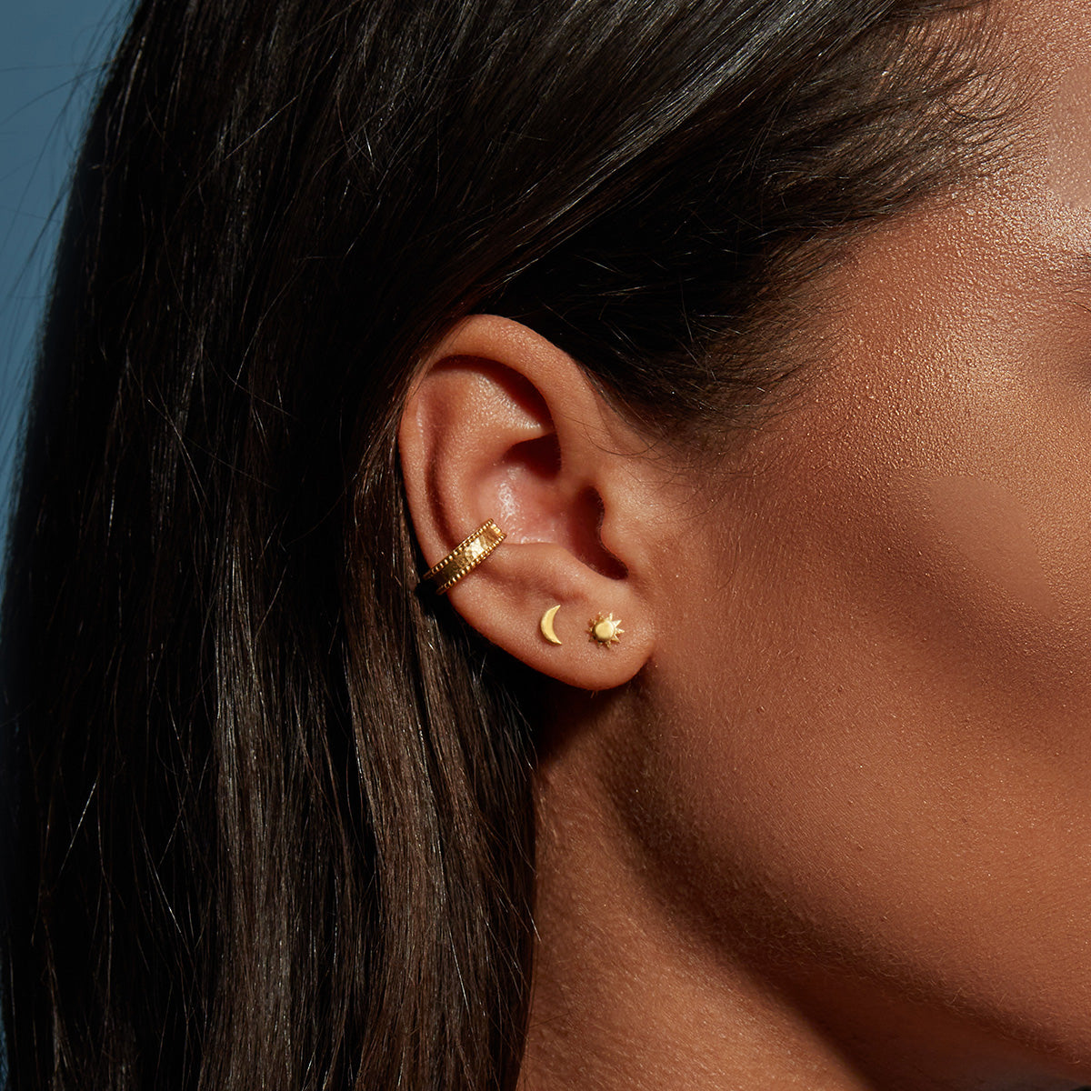 Gold crescent moon and star stud earrings worn on earlobe of person with dark hair.