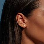 Gold crescent moon and star stud earrings worn on earlobe of person with dark hair.