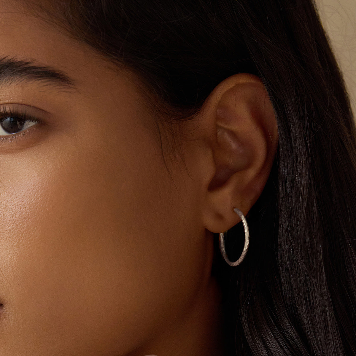 A model wearing Textured Sterling Silver Medium Hoop Earrings, highlighting their elegant design and fit. This pair of hoops serves as a meaningful accent to any outfit and embodies spiritual themes of protection and connection, resonating with the essence of sun and moon motifs.