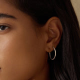 A model wearing Textured Sterling Silver Medium Hoop Earrings, highlighting their elegant design and fit. This pair of hoops serves as a meaningful accent to any outfit and embodies spiritual themes of protection and connection, resonating with the essence of sun and moon motifs.