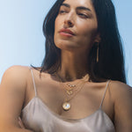 Waking Dreams Mother of Pearl Celestial Necklace worn by a model against a bright sky, symbolizing guidance and goddess energy. This piece of spiritual jewelry serves as a talisman for yoga enthusiasts seeking meaning and manifestation in their practice.