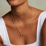 A person wearing the Guiding Hand Mini Hamsa Necklace, showcasing its 18kt gold plated design layered with other spiritual jewelry, symbolizing meditation, protection, and meaningful charms for manifestation.