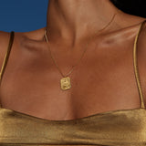 Gold-toned rectangular pendant necklace with Ganesha deity relief, worn on thin chain at chest level.