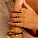 A close-up of a person's hands adorned with various rings, including the Manifesting Dreams White Topaz Petal Ring, surrounded by bracelets that symbolize spiritual jewelry, meditation, and protection, embodying the meaning of transformation and manifestation.
