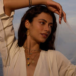 A beautiful woman showcasing multiple layers of spiritual jewelry, including the Inner Knowing Labradorite Snake Necklace, capturing a bohemian vibe. This meditative jewelry collection brings together elements of the sun, moon, and zodiac, symbolizing deep meaning and powerful manifestation.