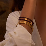 The Loving Protection Garnet Evil Eye Bracelet styled elegantly with additional bracelets, showcasing the gleam of gold accents. This spiritual jewelry promotes grounding energy, making it a perfect fit for meditation and symbolism in protection, meaningful for yoga and zodiac enthusiasts.