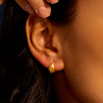 Detailed shot of a hand placing the Little Joys Dot Huggie Hoop Earrings on the ear. These earrings serve as a talisman for meaningful moments, complementing your yoga practice and enhancing your spiritual journey.