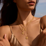 An elegant shot of a woman draped in multiple gold necklaces, including the Shifting Consciousness Snake Necklace. This spiritual jewelry embodies immortality and rebirth, making it a cherished talisman for meditation, protection, and meaningful spiritual growth aligned with the sun and moon.