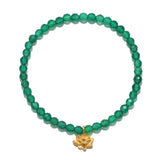 A circular stretch bracelet of small faceted green beads has a matte gold lotus flower charm hanging at the bottom.