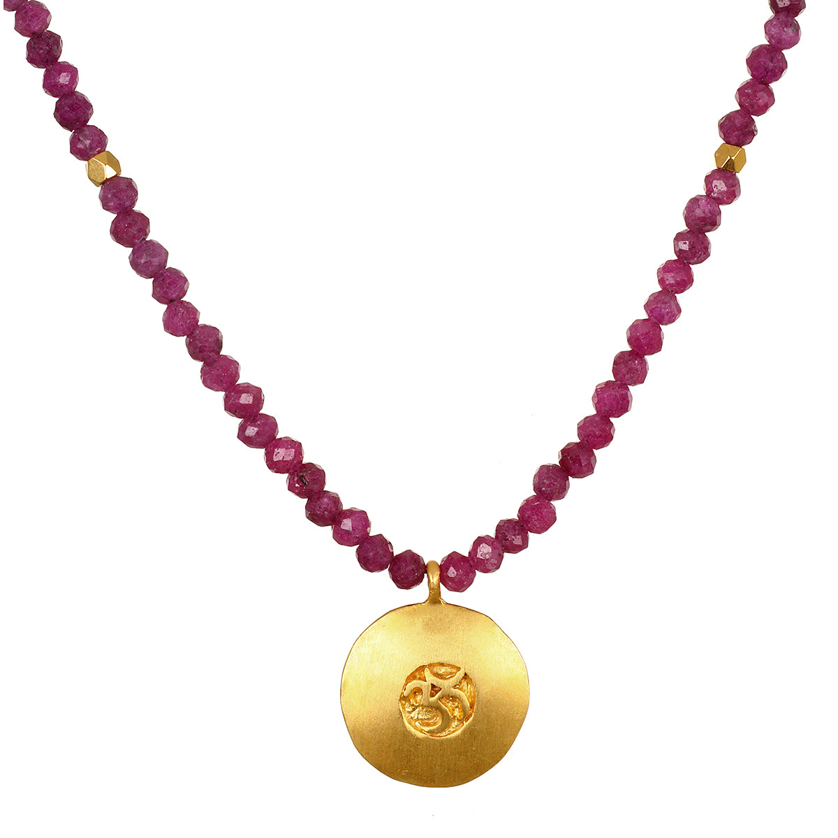 A necklace of faceted deep pink ruby beads with small gold accents holds a round matte gold pendant stamped with an Om symbol.