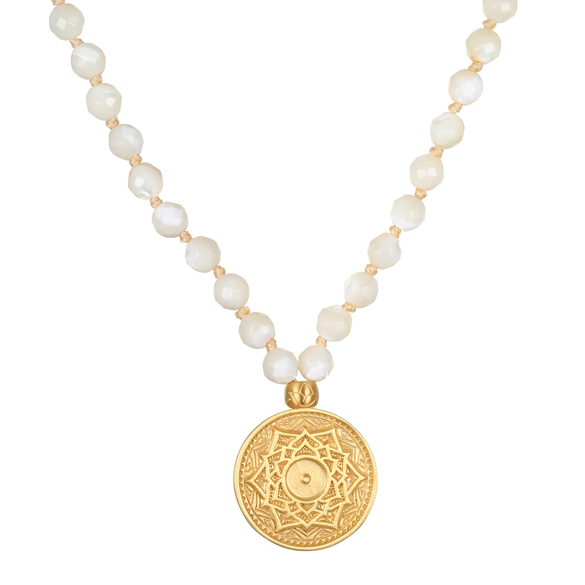A necklace of faceted white pearl beads knotted on cream cord holds a round gold pendant engraved with a lotus mandala design.