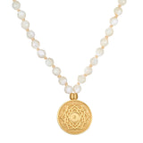 A necklace of faceted white pearl beads knotted on cream cord holds a round gold pendant engraved with a lotus mandala design.