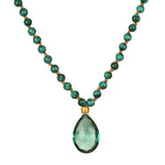 A necklace of round green malachite beads knotted on tan cord holds a faceted teardrop green gemstone pendant with a gold cap.