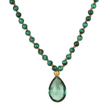 A necklace of round green malachite beads knotted on tan cord holds a faceted teardrop green gemstone pendant with a gold cap.