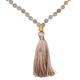 A necklace of faceted grey beads with small knots between them ends in a gold-toned bead and a long taupe silk tassel.