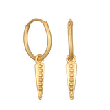 A pair of matte gold hoop earrings, each with a dangling triangular dagger charm decorated with a vertical row of small beads.